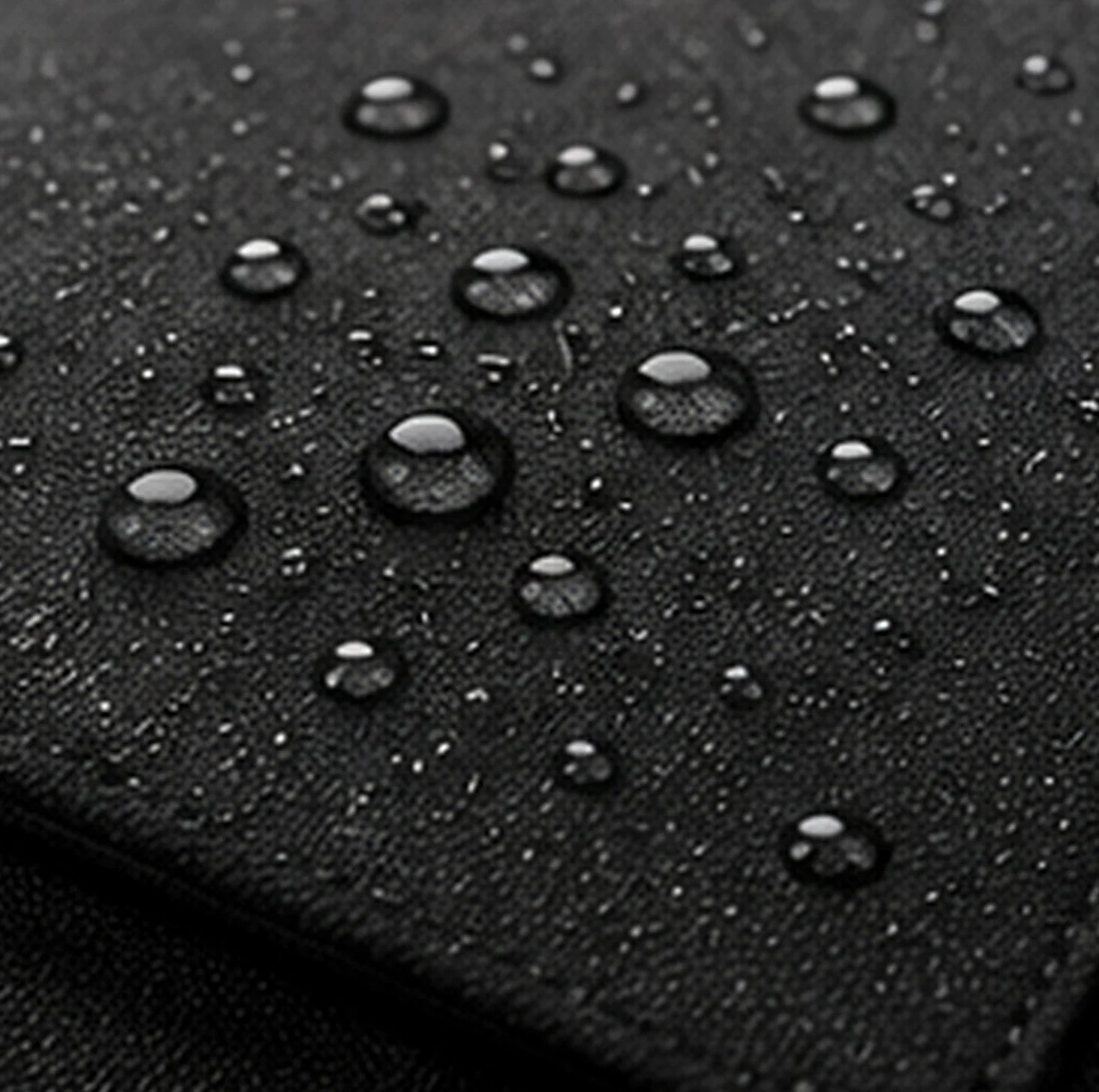 Water beading on the textured black fabric of a DRAEN backpack